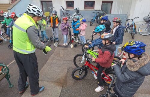 Kinder stehen mit ihren Rollern und Rädern bereit