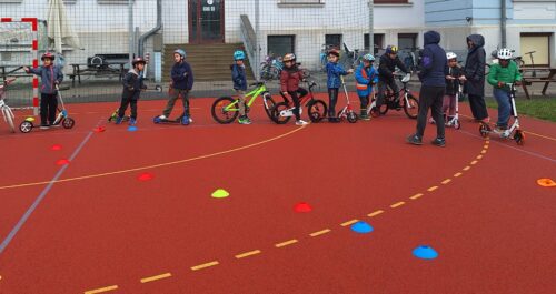 Kinder stehen mit ihren Rollern und Rädern bereit