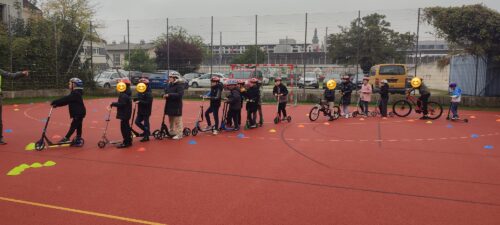 Kinder stehen mit Rollern und Fahrrädern in einer Reihe