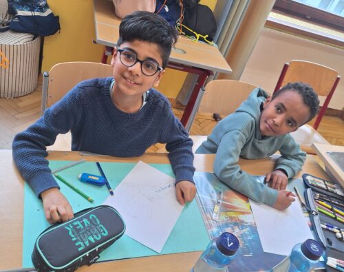 Zwei Buben sitzen am Platz und gestalten ihre nachgespurten Hände