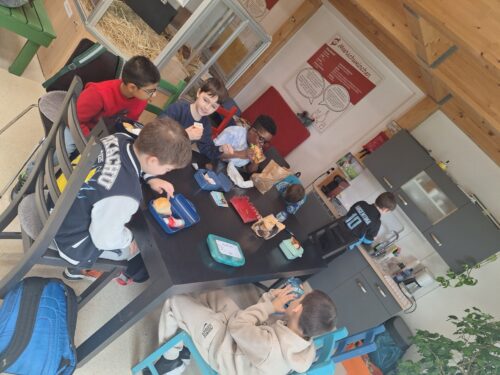 Kinder sitzen um den Tisch und essen ihre Jause