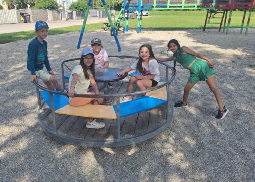 Kinder sitzen im Ringelspiel am Spielplatz