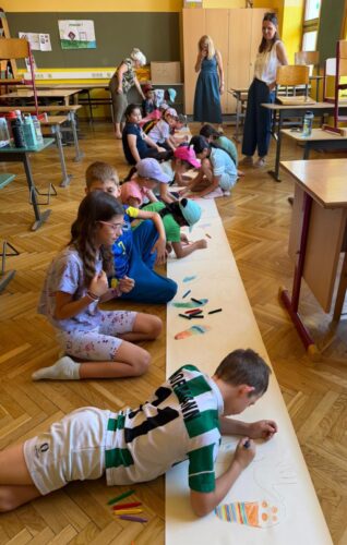 Kinder liegen am Boden und malen auf einem großen Plakat