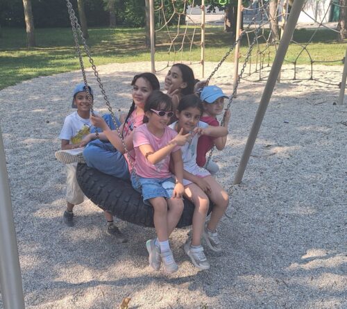 Kinder sitzen am Spielplatz in einer Reifenschaukel