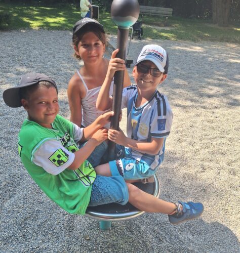 Kinder sitzen auf einem Spielgerät am Spielplatz