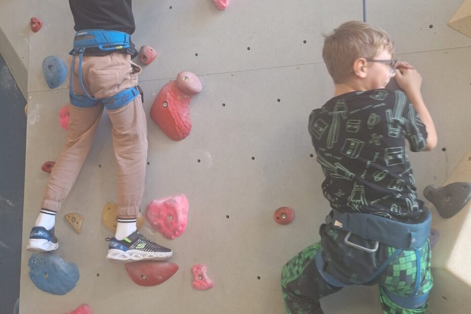 2 Kinder klettern mit Klettergeschirr auf einer Kletterwand