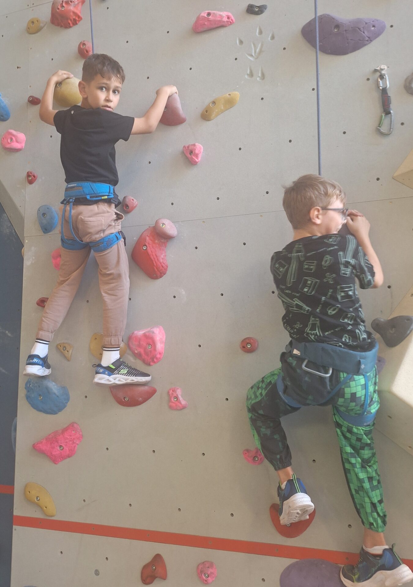 2 Kinder klettern mit Klettergeschirr auf einer Kletterwand