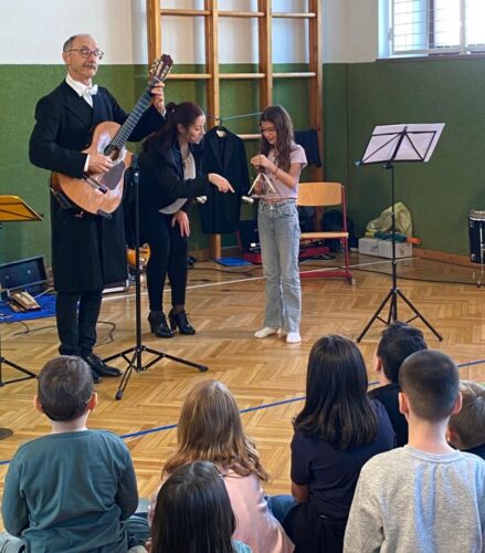 Ein Mann spielt Gitarre und eine Frau zeigt einem Mädchen wie man die Triangel spielt
