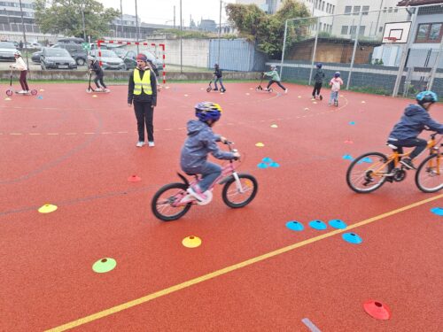Die Kinder fahren mit den Rädern und Rollern den aufgebauten Parcour am Hartplatz