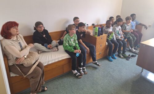 Die Kinder sitzen auf 2 Betten und hören den Vortragenden zu