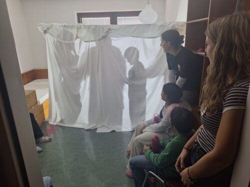 Kinder spielen ein Schattenspiel hinter einem Leintuch