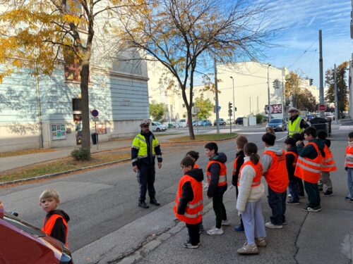 Zwei Polizisten erklären den Schülern und Schülerinnen das richtige Verhalten beim Überqueren der Straße.