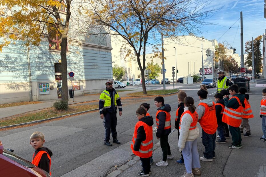 Zwei Polizisten erklären den Schülern und Schülerinnen das richtige Verhalten beim Überqueren der Straße.
