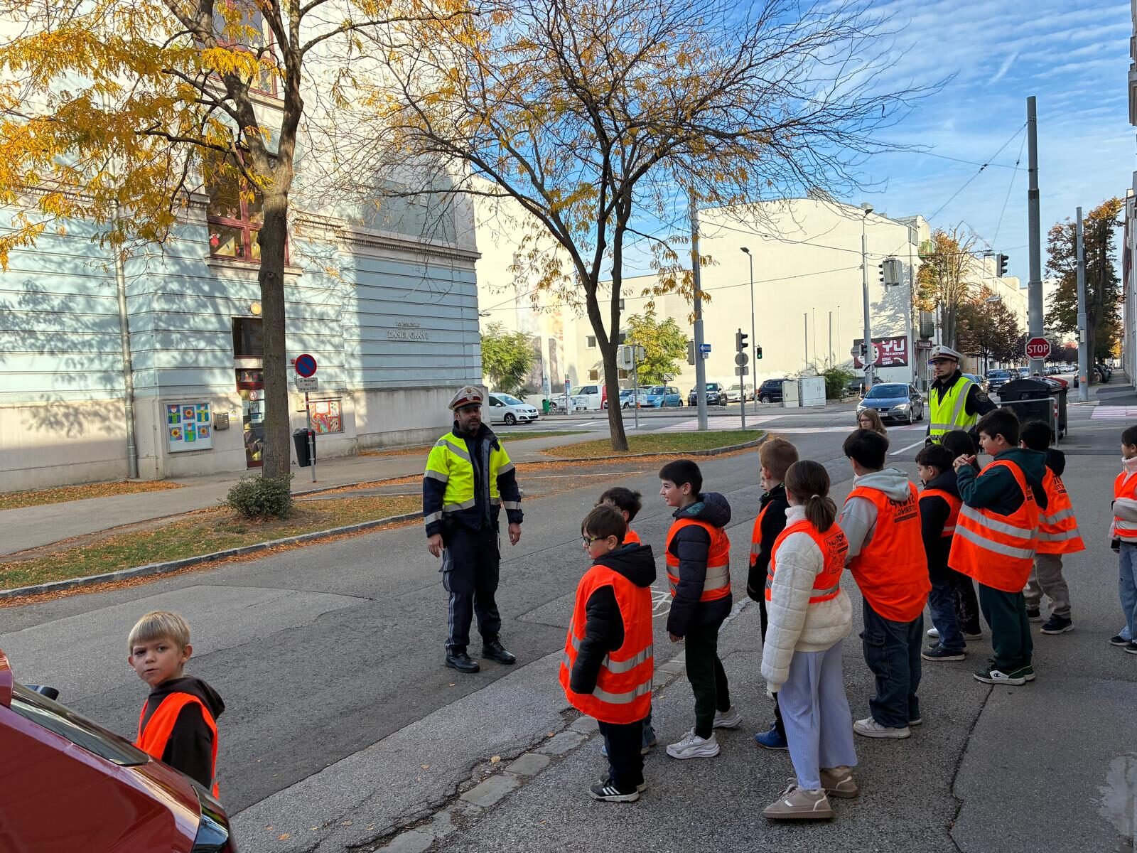 Zwei Polizisten erklären den Schülern und Schülerinnen das richtige Verhalten beim Überqueren der Straße.